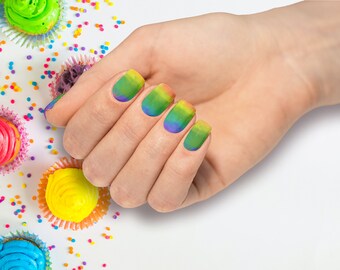 May include: A hand with rainbow ombre nail polish. The nails are painted in shades of green, blue, yellow, and orange. The hand is surrounded by colorful sprinkles.