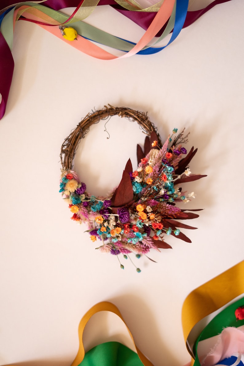 May include: A dried flower wreath with a variety of colors, including purple, pink, orange, and blue. The wreath is made of twigs and is decorated with dried flowers and leaves.