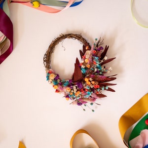 May include: A dried flower wreath with a variety of colors, including purple, pink, orange, and blue. The wreath is made of twigs and is decorated with dried flowers and leaves. The wreath is surrounded by colorful ribbons.