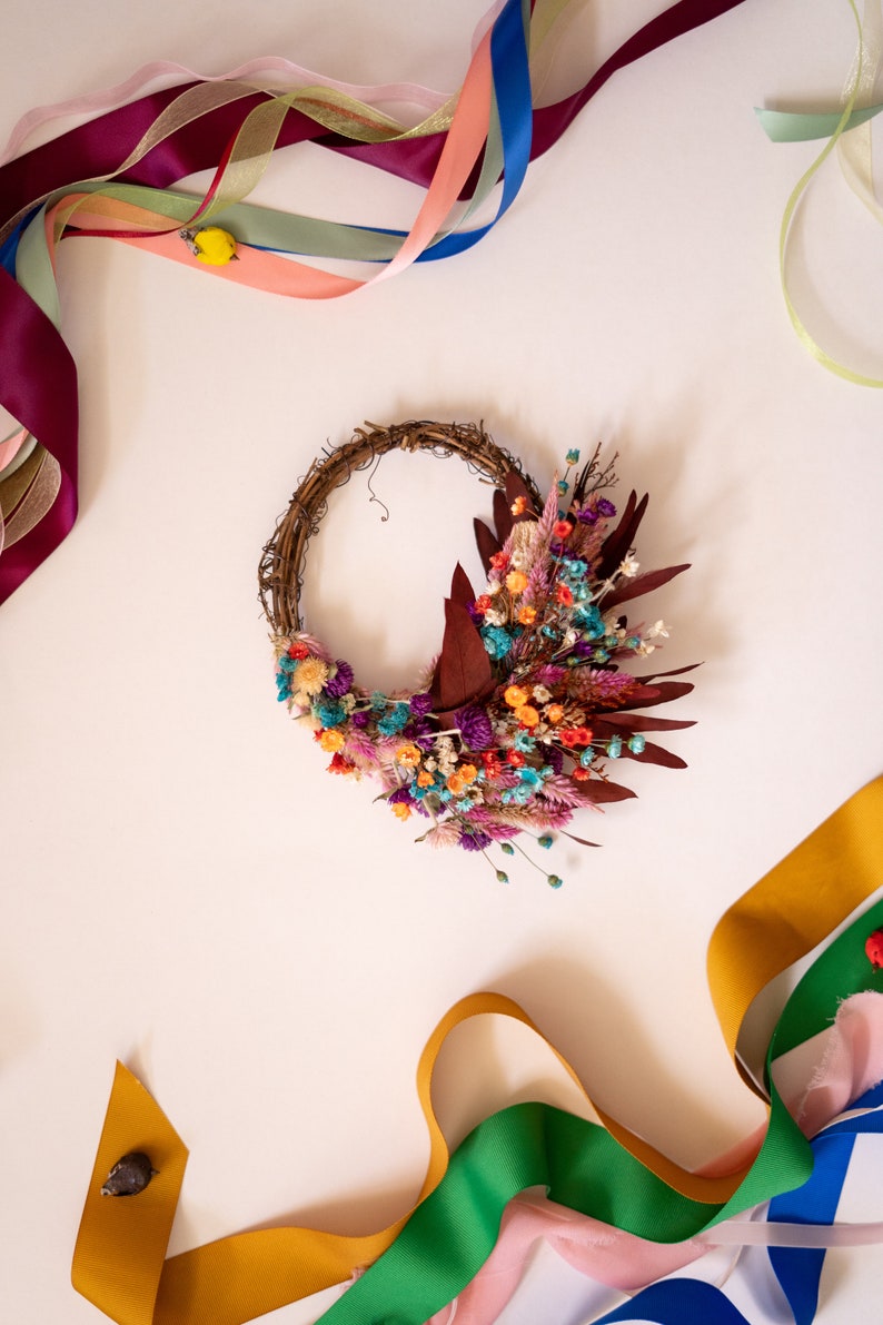 May include: A dried flower wreath with a variety of colors, including purple, pink, orange, and blue. The wreath is made of twigs and is decorated with dried flowers and leaves. The wreath is surrounded by colorful ribbons.