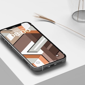 May include: A black smartphone with a geometric patterned wallpaper in shades of brown, white, and orange. The screen displays "Samedi 28 octobre 08:00". A slender, dried plant stem and a clear vase are in the background.