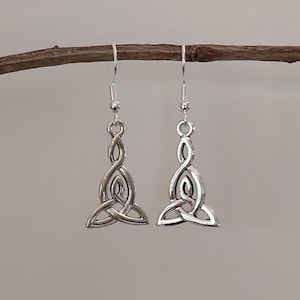 May include: A pair of silver-colored Celtic knot earrings. Each earring features a stylized, intertwined design, suspended from a simple hook. The earrings are displayed against a neutral background, highlighting their intricate details and metallic sheen.