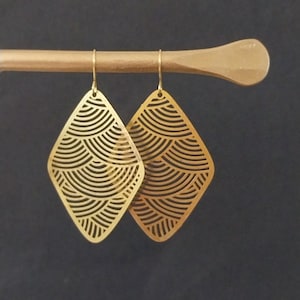 May include: A pair of gold-tone earrings with a geometric diamond shape and a patterned design. The earrings are made of metal and have a delicate, intricate design.