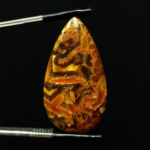 Op de afbeelding: Een traanvormige cabochon van agaat met een bruin, oranje en geel patroon. De agaat is doorschijnend en heeft een glanzende afwerking.