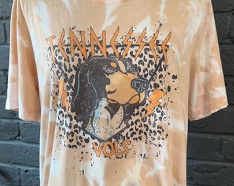 Puede incluir: Una camiseta naranja y blanca tie-dye con un estampado gráfico de la cabeza de un perro con el texto "Tennessee Vols" debajo.