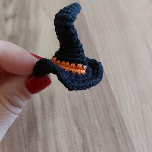 Op de afbeelding: Een kleine zwarte gehaakte heksenhoed met een oranje rand.