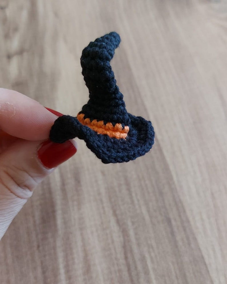 Op de afbeelding: Een kleine zwarte gehaakte heksenhoed met een oranje rand.