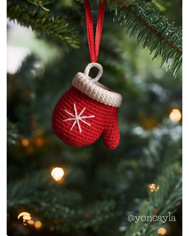 May include: A red crocheted mitten ornament with a white snowflake design hanging from a red ribbon on a green Christmas tree.