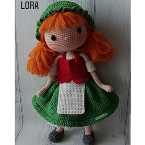 May include: A crocheted doll with red hair, a green hat, a red and white dress, and green shoes. The doll is named Lora.