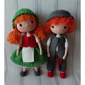 May include: Two crocheted dolls, one wearing a green dress and a red vest, the other wearing a gray vest and pants. Both dolls have red yarn hair.