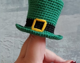 May include: A green crocheted leprechaun hat with a black band and a yellow buckle. The hat is worn on a finger.