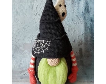 May include: A crocheted gnome wearing a black witch hat with a white spiderweb design. The gnome has a green beard and red mittens. A white ghost is peeking out from under the hat.