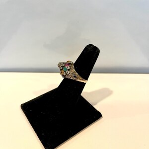May include: A silver ring with a cluster of colorful gemstones set in a floral design. The ring is displayed on a black ring stand.