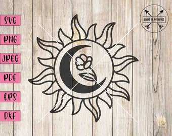 Puede incluir: Diseño en blanco y negro de línea de arte de un sol con una luna creciente en su interior. Una pequeña flor está dentro de la luna. El diseño está sobre un fondo de veta de madera.