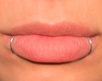 May include: Close-up of a person's lower lip with a silver lip ring piercing.