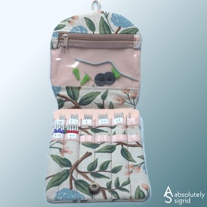 May include: Floral print knitting needle case with a clear zippered pocket and multiple compartments for needles. The case features a pink interior and a button closure. The case is decorated with a floral pattern in shades of blue, green, and pink.