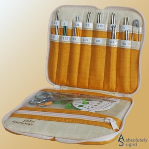 May include: Open, zippered knitting needle case with various sizes of needles, ranging from 2.5 to 5.0. The case is beige and gold, with a clear compartment holding scissors and other tools. The text "absolutely sigrid" is visible.