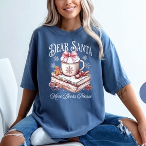 A woman wearing a blue t-shirt with a graphic design of a mug and books, sitting on a white chair.