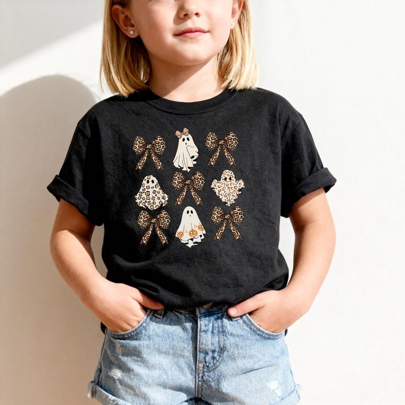 A young girl wearing a black t-shirt with a graphic design of ghostly figures and leopard print elements.