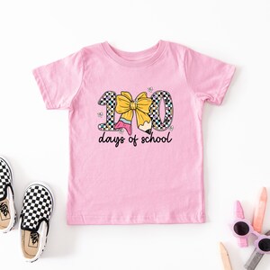 A pink t-shirt with a graphic design, a pair of black and white checkered shoes, and some children's art supplies such as markers and colored pencils.
