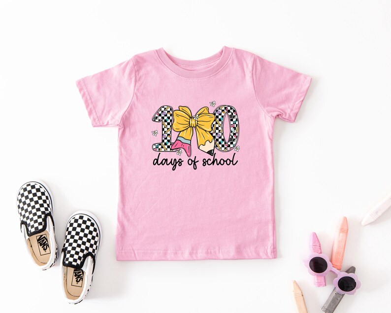 A pink t-shirt with a graphic design, a pair of black and white checkered shoes, and some children's art supplies such as markers and colored pencils.