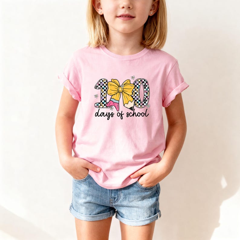 A young girl wearing a pink t-shirt with a graphic design of the number 100 and the text "100 days of school" printed on it.