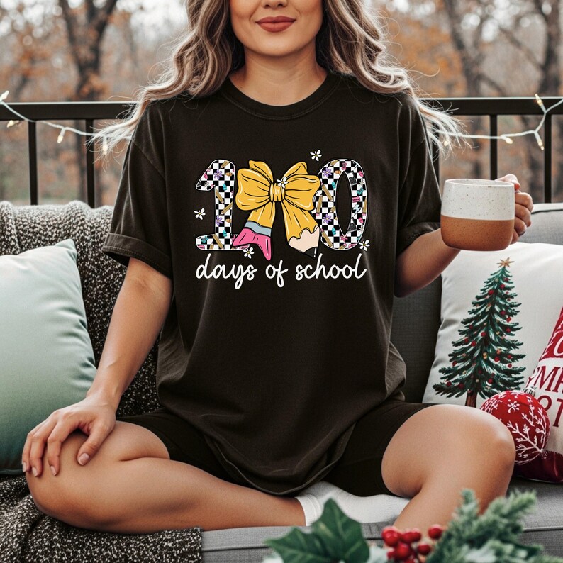 A woman sitting on a couch with a mug in her hand, wearing a black t-shirt with a graphic design.