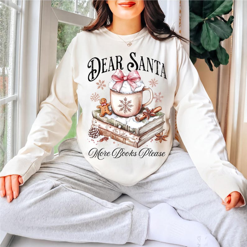 A woman wearing a white sweater with a graphic design of a mug, books, and a snowflake, sitting in a window with a potted plant in the background.