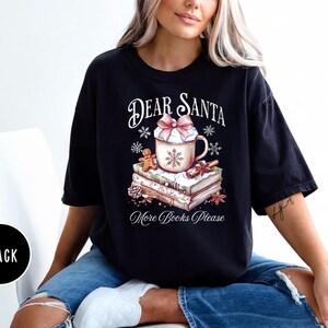 A woman wearing a black t-shirt with a graphic design of a mug and books, sitting on a chair.