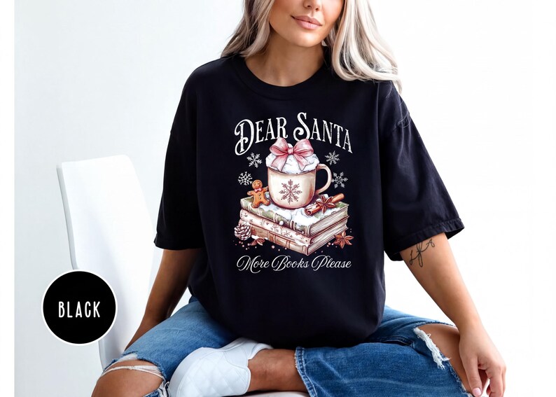 A woman wearing a black t-shirt with a graphic design of a mug and books, sitting on a chair.