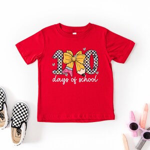 A red t-shirt with a graphic design, a pair of black and white checkered shoes, and some children's sunglasses on a white background.
