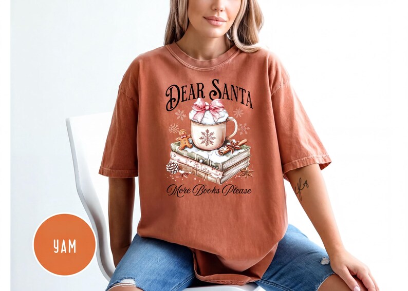 A woman wearing a t-shirt with a Christmas-themed design, including a mug, books, and snowflakes.