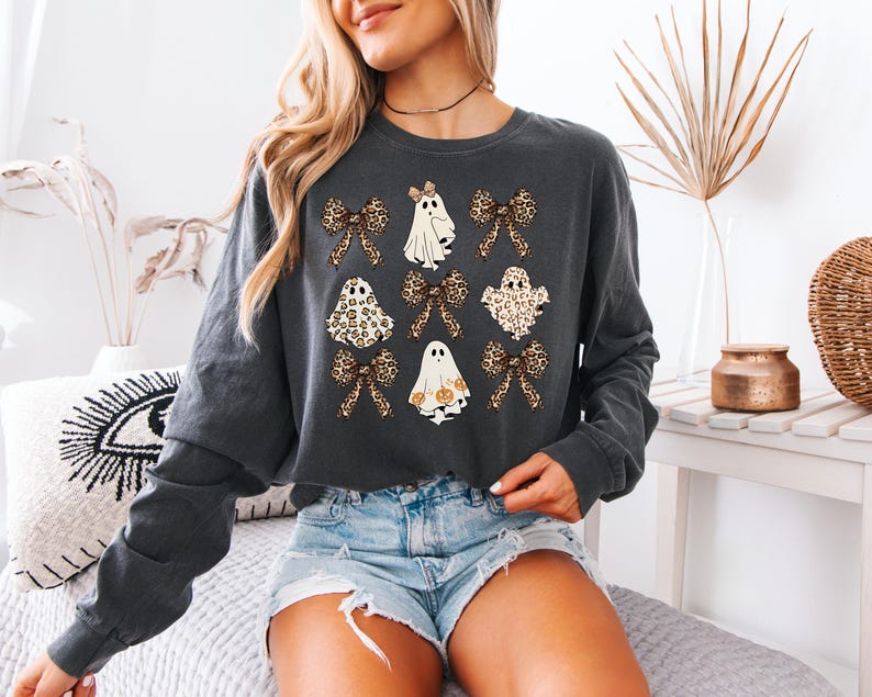 A woman wearing a gray sweatshirt with a graphic design of ghostly figures and leopard-print bows, paired with denim shorts.