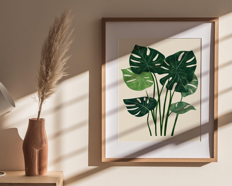 May include: A framed print of a watercolor illustration of a green monstera plant on a cream background.