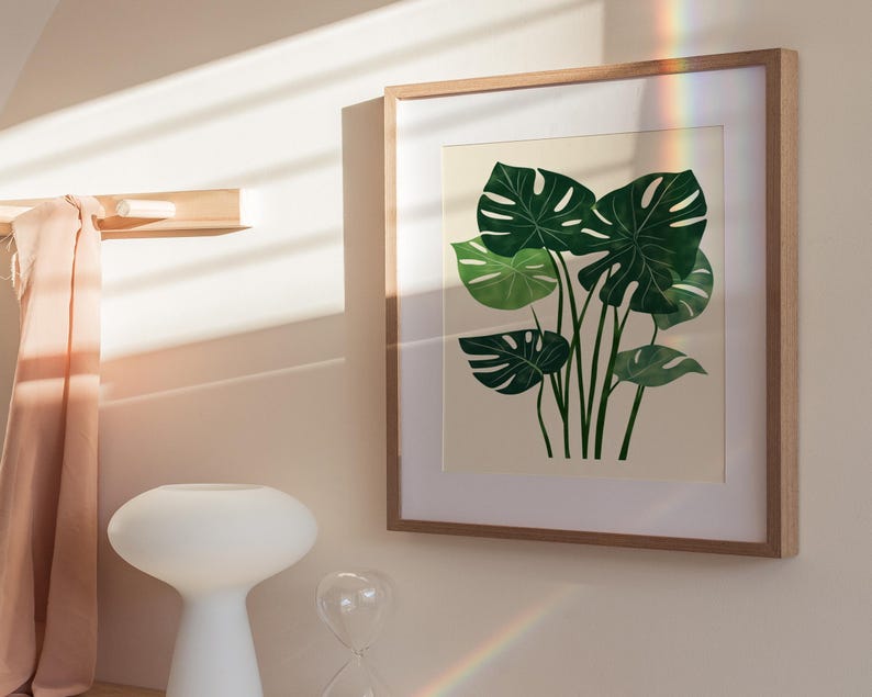 May include: A framed print of a botanical illustration featuring a cluster of green monstera leaves on a cream background.