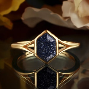 May include: A gold ring with a dark blue hexagonal gemstone. The gemstone has a sparkly, textured surface.
