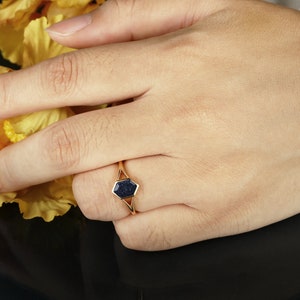 May include: A gold ring with a dark blue hexagonal stone set in a geometric design.