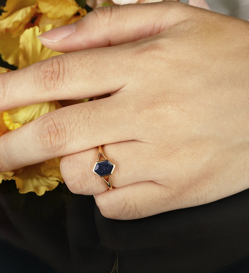 May include: A gold ring with a dark blue hexagonal stone set in a geometric design.