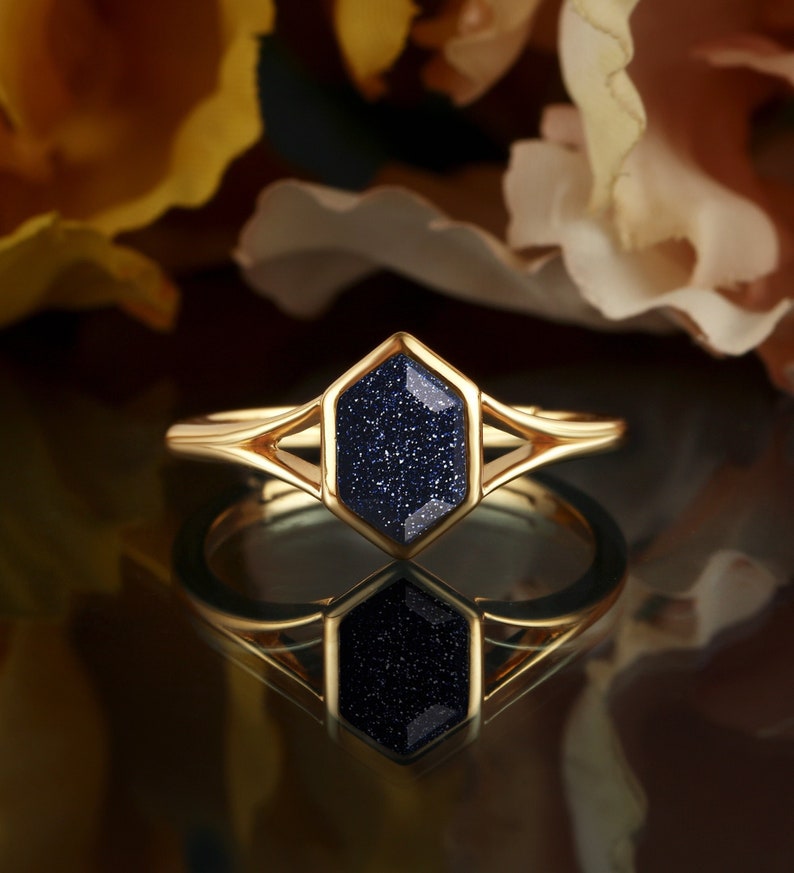 May include: A gold ring with a dark blue hexagonal gemstone. The gemstone has a sparkly, textured surface.