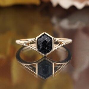 May include: Gold ring with a black hexagonal gemstone. The gemstone has a sparkly, speckled texture.