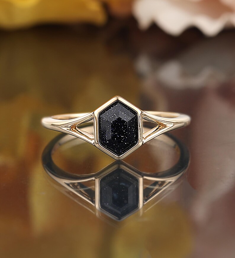 May include: Gold ring with a black hexagonal gemstone. The gemstone has a sparkly, speckled texture.