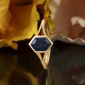 May include: A gold ring with a hexagonal blue stone set in the center. The stone has a sparkly, textured surface.