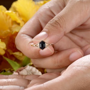 May include: A gold ring with a black octagon-shaped gemstone. The ring is set with a delicate, double-prong setting.