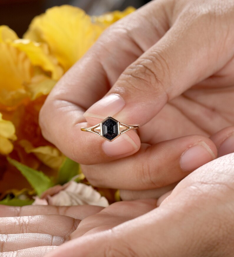 May include: A gold ring with a black octagon-shaped gemstone. The ring is set with a delicate, double-prong setting.