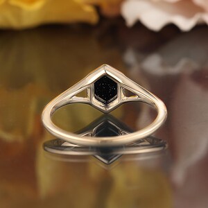 May include: A gold ring with a black hexagonal stone set in a geometric design.