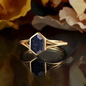 May include: Gold ring with a blue gemstone set in a hexagonal shape. The ring has a delicate, open design.