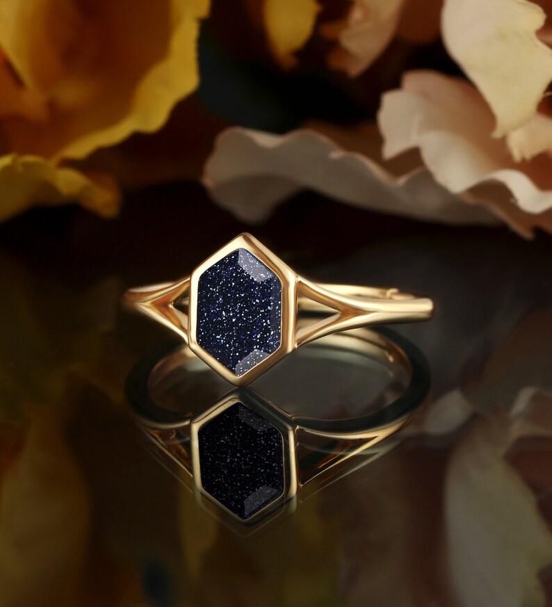 May include: Gold ring with a blue gemstone set in a hexagonal shape. The ring has a delicate, open design.