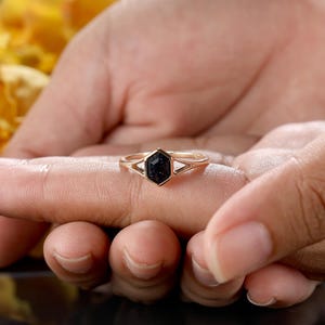 May include: A gold ring with a black hexagonal stone set in a geometric design.