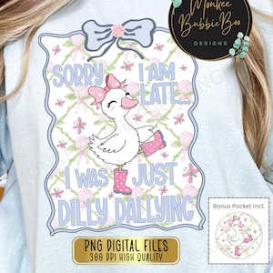 May include: A light blue t-shirt with a white and pink design featuring a cartoon duck wearing pink rain boots and a pink bow. The text "Sorry I am late... I was just dilly dallying" is printed on the shirt. The shirt also includes a bonus pocket design with a similar duck design.