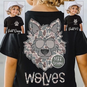 May include: Black t-shirt featuring a wolf design with sunglasses and the word "wolves" in a camouflage pattern. The shirt also has a small paw print design and the text "Pocket Design" on the front.